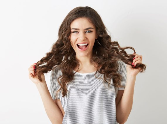 attractive young lady holding her long brown curly hair laughing with positive face expression, emotional woman, looking in camera, isolated, happy emotion